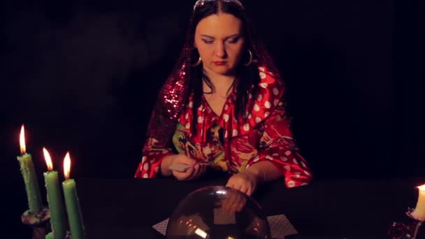 Gypsy fortune teller at the table by candlelight spreads fortunetelling cards. — Stock Video
