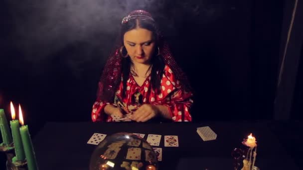 Um cartomante cigano à mesa à luz das velas lê o futuro nas cartas na fumaça — Vídeo de Stock