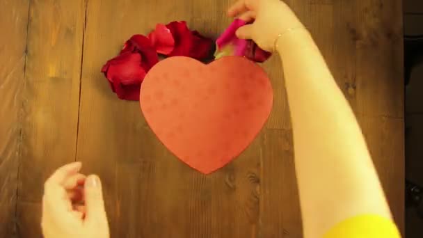 La muchacha pone el corazón sobre la mesa de madera de los pétalos de rosa. Vueltas de tiempo — Vídeos de Stock