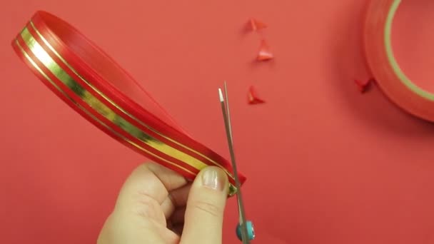 As mãos das mulheres cortam os cantos de uma fita vermelha em branco com um par de tesouras para fazer um arco de presente. Fundo vermelho — Vídeo de Stock