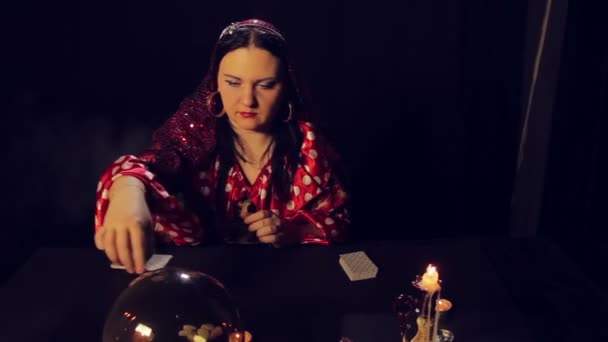 Une diseuse de bonne aventure gitane à table aux chandelles lit l'avenir sur les cartes dans la fumée — Video