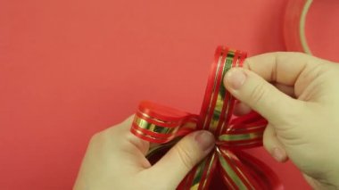Kadın el bir pembe kurdele hediye yay yaprakları düzeltmek. Kırmızı bir arka plan