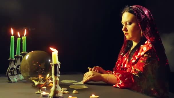 A young gypsy in a fortune-telling saloon by candlelight lays out cards for divination on the table — Stock Video