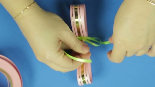 Las manos de las mujeres están atadas con una trenza rosa con un blanco rosado para un lazo de regalo. Fondo azul — Vídeos de Stock