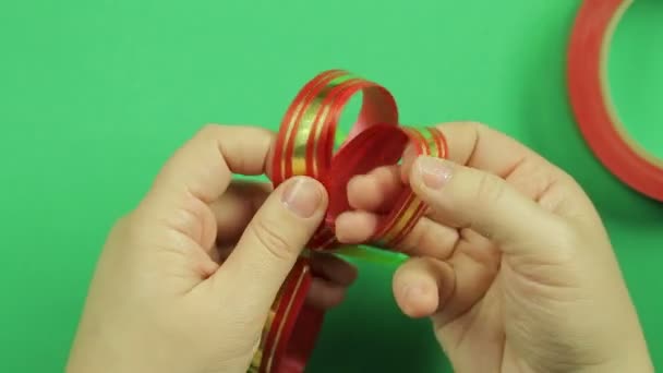 Γυναικεία χέρια ισιώσει τα πέταλα του μια κόκκινη κορδέλα τόξο δώρο. Πράσινο φόντο — Αρχείο Βίντεο