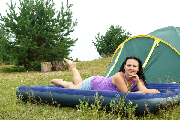 Joven morena descansando sobre un colchón inflable en la tienda sobre la hierba verde . —  Fotos de Stock