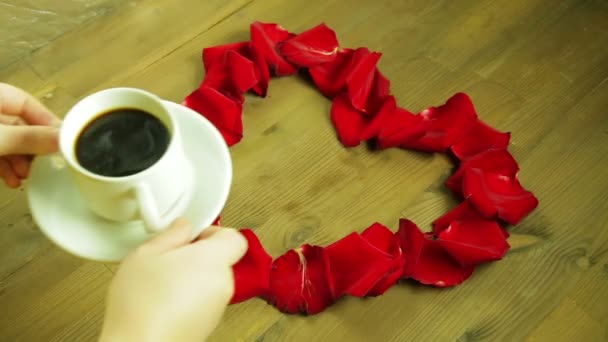 A menina coloca no meio do coração das pétalas de rosa uma xícara de café — Vídeo de Stock