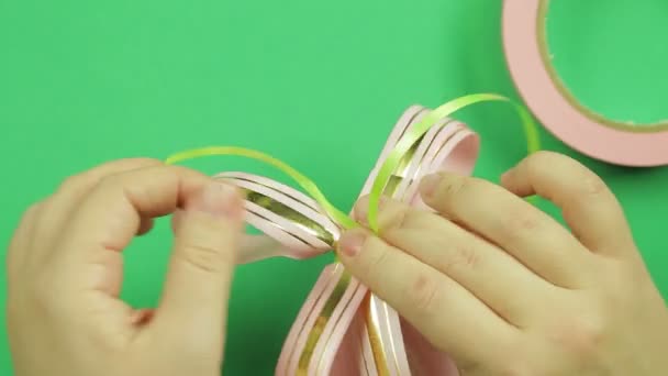 Female hands give shape to a pink ribbon bow on a green background — Stock Video