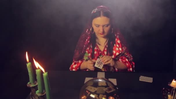 Цыганский гадалка за столом при свечах читает будущее на картах в дыму — стоковое видео