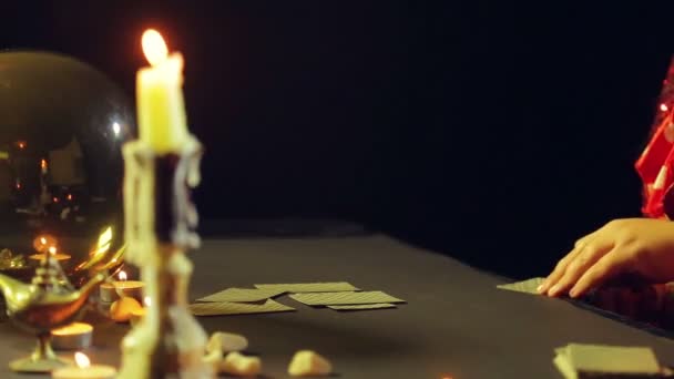 Um jovem cigano em um salão de adivinhação à luz de velas expõe cartas para adivinhação na mesa . — Vídeo de Stock
