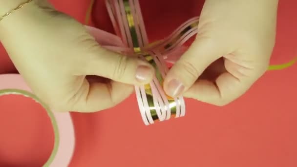 Womens hands straighten the petals of the gift ribbon bow from the pink ribbon. Red background — Stock Video