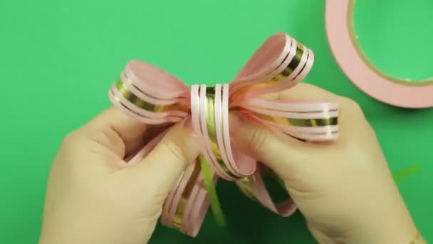 Female hands give shape to a pink ribbon bow on a green background — Stock Video