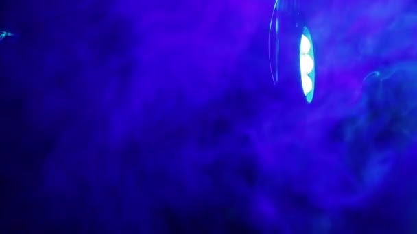 Έναν προβολέα που εκπέμπουν σε πολύχρωμες ακτίνες σε ένα σύννεφο καπνού αυτοκίνητα. Μαύρο φόντο — Αρχείο Βίντεο
