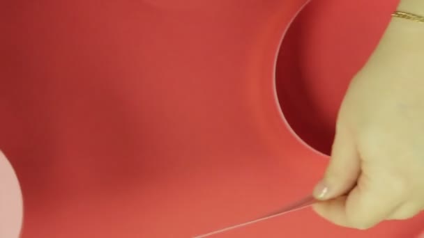Жіночі руки вимірюють рожеву стрічку для виготовлення подарункового лука. Червоний фон . — стокове відео