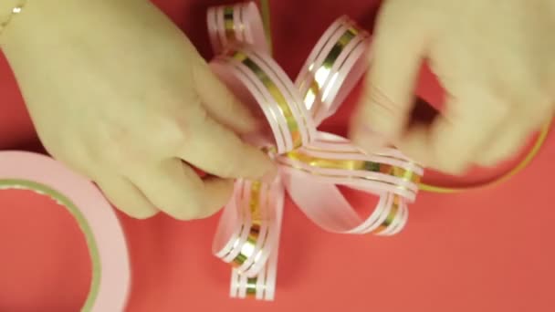 Womens hands straighten the petals of a pink ribbon gift bow and give it the shape of a bow. Red background — Stock Video