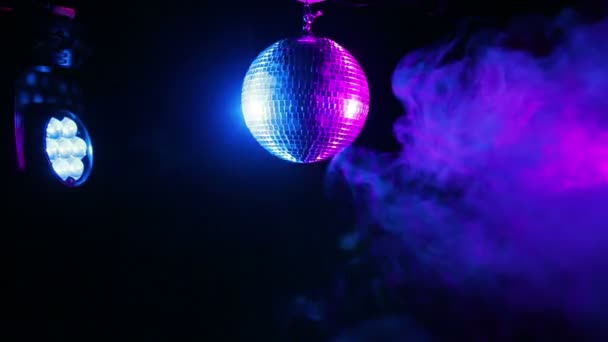 Espelho bola para discoteca em um fundo preto nos raios de holofotes e nuvens de fumaça colorida — Vídeo de Stock