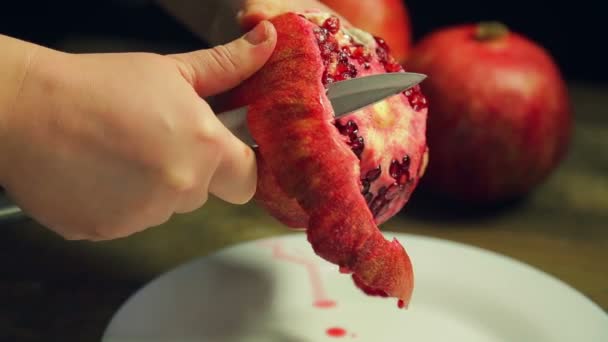 Mujer limpia fruta de granada con un cuchillo en un plato blanco en una mesa de madera . — Vídeos de Stock
