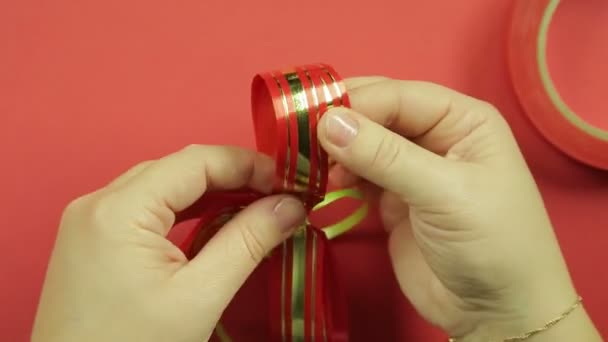 Las manos de mujer enderezan los pétalos de un lazo de regalo de cinta rosa. Fondo rojo — Vídeos de Stock