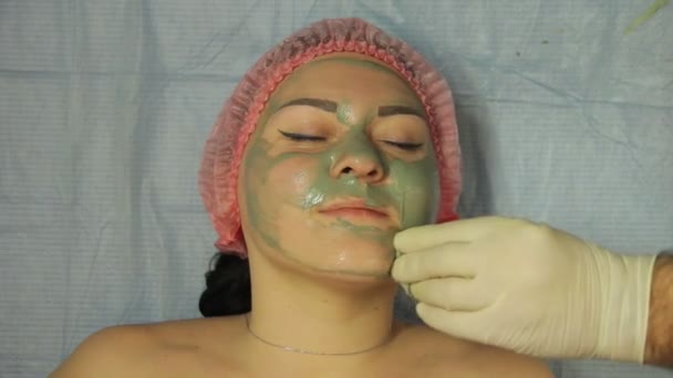 De cosmeticaspecialisten-handen in handschoenen verwijderen de modder masker uit het gezicht van de vrouw met een wattenschijfje — Stockvideo