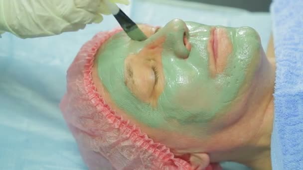 Een vrouwelijke schoonheidsspecialist geldt een genezende modder masker voor een man s gezicht met een borstel. Zijaanzicht — Stockvideo