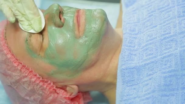 Een vrouwelijke schoonheidsspecialist verwijdert een therapeutische modder masker uit de s gezicht van een man met een wattenschijfje. Zijaanzicht — Stockvideo