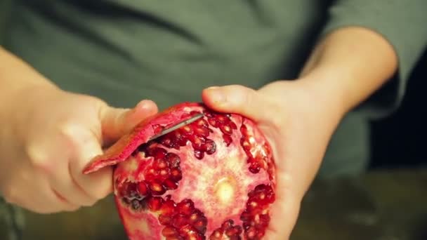 Vrouw reinigt granaatappel fruit met een mes op een witte plaat op een houten tafel — Stockvideo