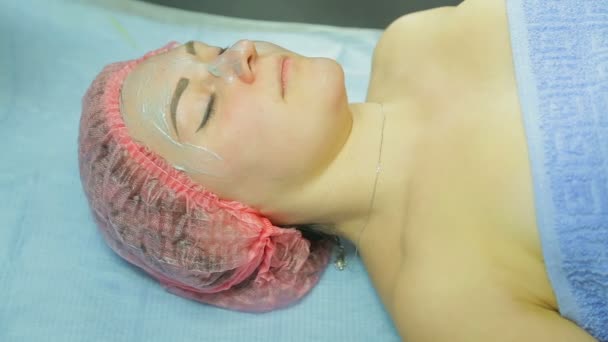 Un cosmetician în mănuși cu o perie aplică o mască de noroi pe fața unei femei. Vedere laterală — Videoclip de stoc