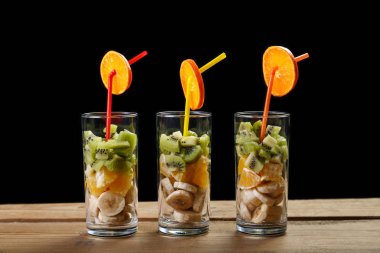 siyah zemin ahşap bir masa üzerinde meyve parçaları olan bardaklar