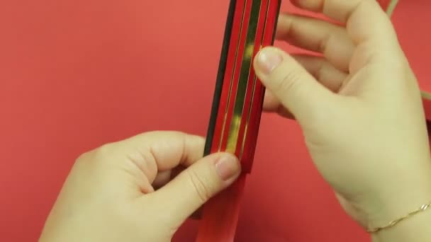 Female hands wrapping a red ribbon template for making a gift bow. Red background — Stockvideo