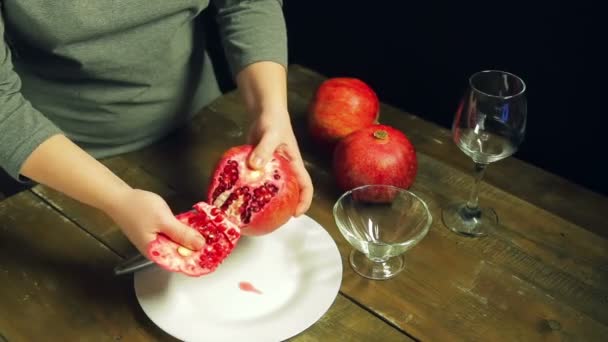 Woman cleans pomegranate fruit on a white plate on a wooden table — Stock Video