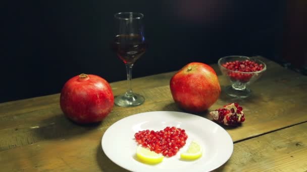 El corazón de las semillas de granada en un plato blanco decorado con rodajas de limón. Sobre la mesa hay granadas frescas y un vaso de jugo de granada. — Vídeo de stock