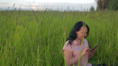 Yeşil çim oturan ve Park planı arasında tablet üzerinde çalışan gülümseyen kadın