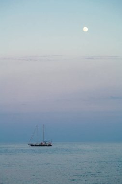Denizde akşam alacakaranlıkta bir yelken ile küçük bir yat.