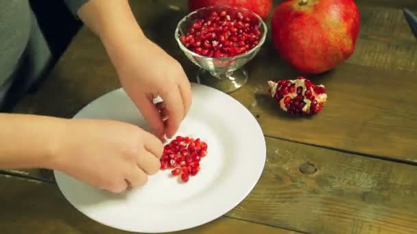 Vrouwelijke handen verdeeld hart uit granaatappel zaden op een witte plaat. — Stockvideo