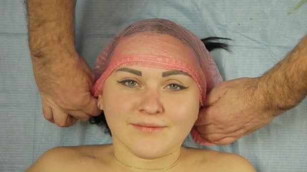 Руки косметолога в перчатках надели косметическую шляпу на женскую голову. — стоковое видео