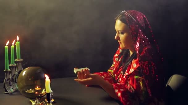 Um jovem cigano em um salão de adivinhação à luz de velas cobra cartões para adivinhação — Vídeo de Stock