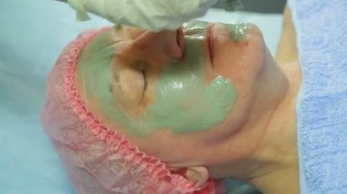 Eldiven kadın bir güzellik uzmanı bir adam s yüz fırçası ile tedavi kil maskesi uygulandığı