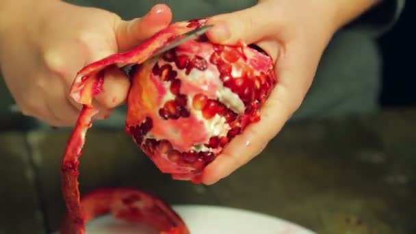 Frau putzt Granatapfelfrucht mit Messer auf weißem Teller auf Holztisch — Stockvideo