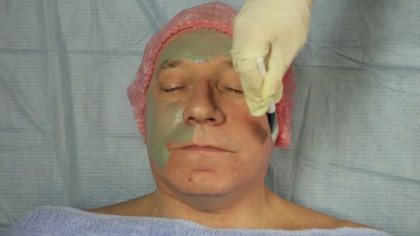 Ženské kosmetička v rukavicích klade na mans tvář bahenní maska — Stock video
