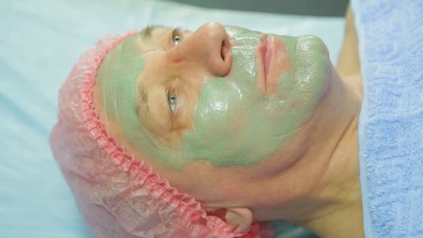 Una cosmetologa donna applica una maschera di fango al viso di un uomo con un pennello. Vista laterale . — Video Stock