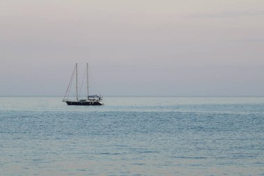 Denizde akşam alacakaranlıkta bir yelken ile küçük bir yat.
