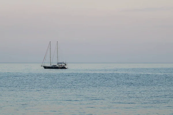 A small yacht with a sail in the sea at dusk in the evening.