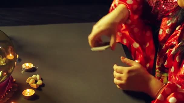 Молодой цыган в красном платье за столом при свечах читает будущее с гадалками — стоковое видео