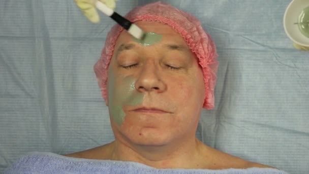 Le mani di un cosmetologo rimuovono una maschera di fango dal viso di un uomo con un batuffolo di cotone — Video Stock