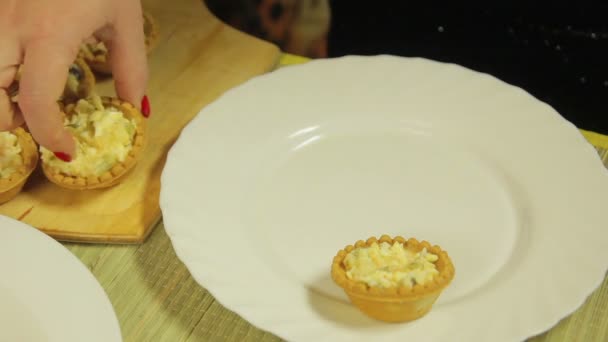 Жінка кладе тарталетки з салатом на білу тарілку — стокове відео
