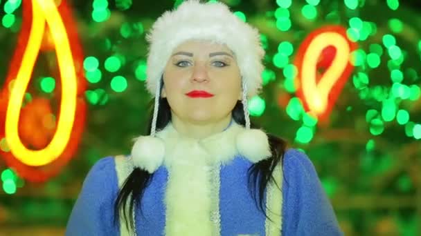 A smiling snow maiden shows a heart at the Christmas tree — Stock Video