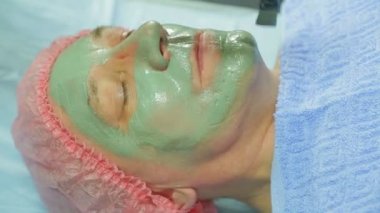 Kadın güzellik uzmanı bir adam s yüz fırçası ile şifalı çamur maskesi uygular. Yan görünüm.