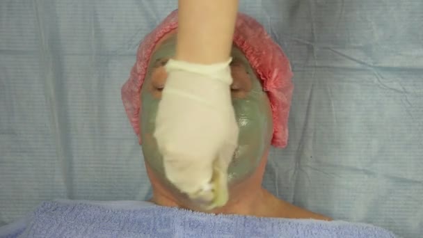 Een vrouwelijke schoonheidsspecialist in handschoenen is de toepassing van een modder masker op het gezicht van een mannelijke client — Stockvideo