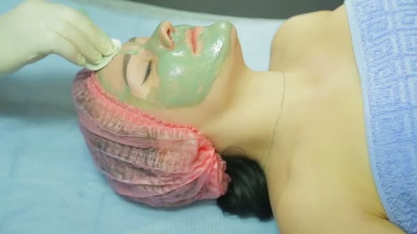A beautician in gloves removes a clay mask from a woman s face with a cotton pad. Side view — Stock Video