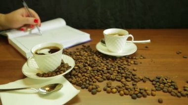 Güçlü kahve fincan, kahve çekirdekleri tablo ve bir kadın bir saçılma bir günlüğüne yazar.